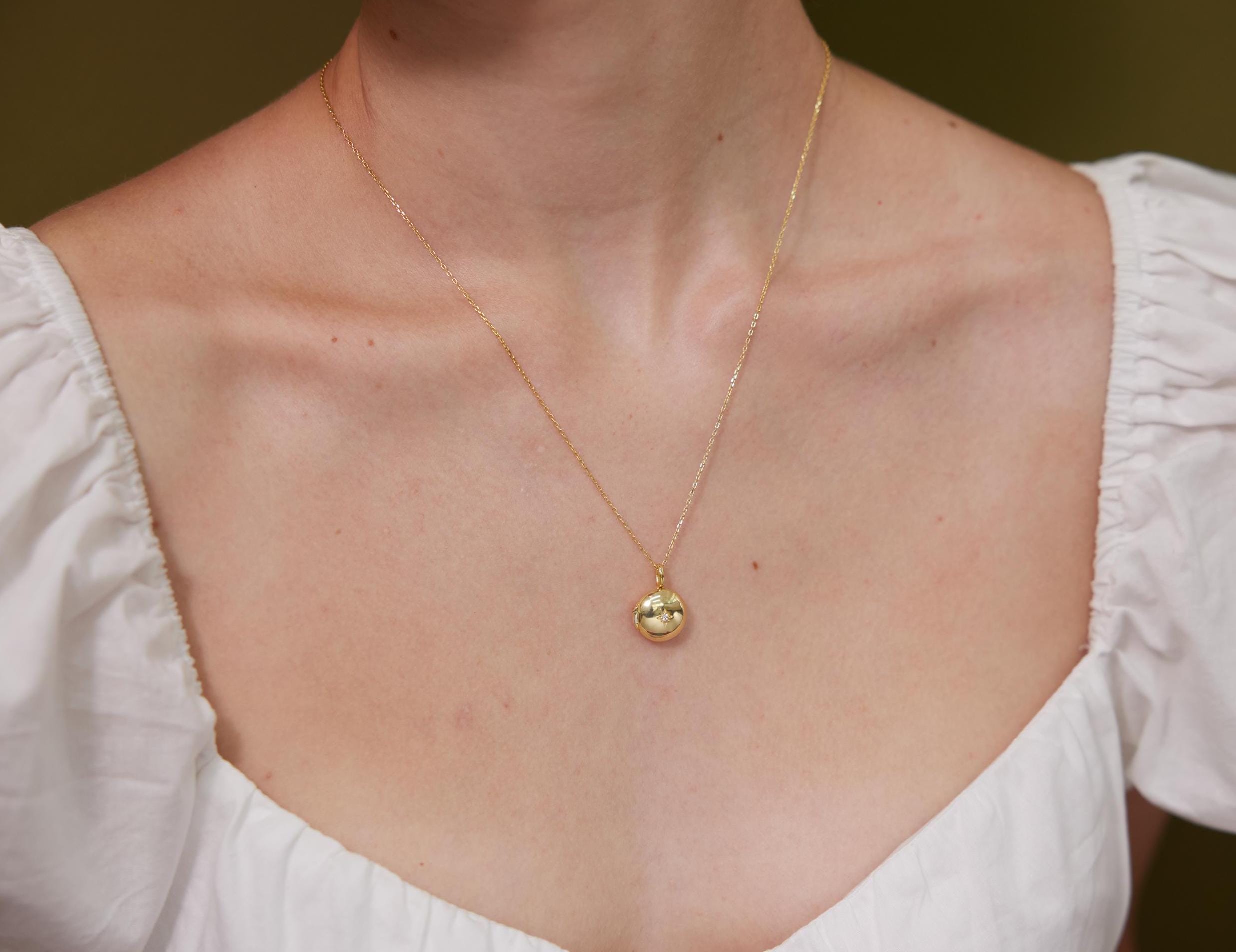 Gold necklace with a pendant on a person wearing a white blouse against a neutral background