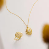 a gold necklace and a gold ring with a sunburst design, both placed on a white background.