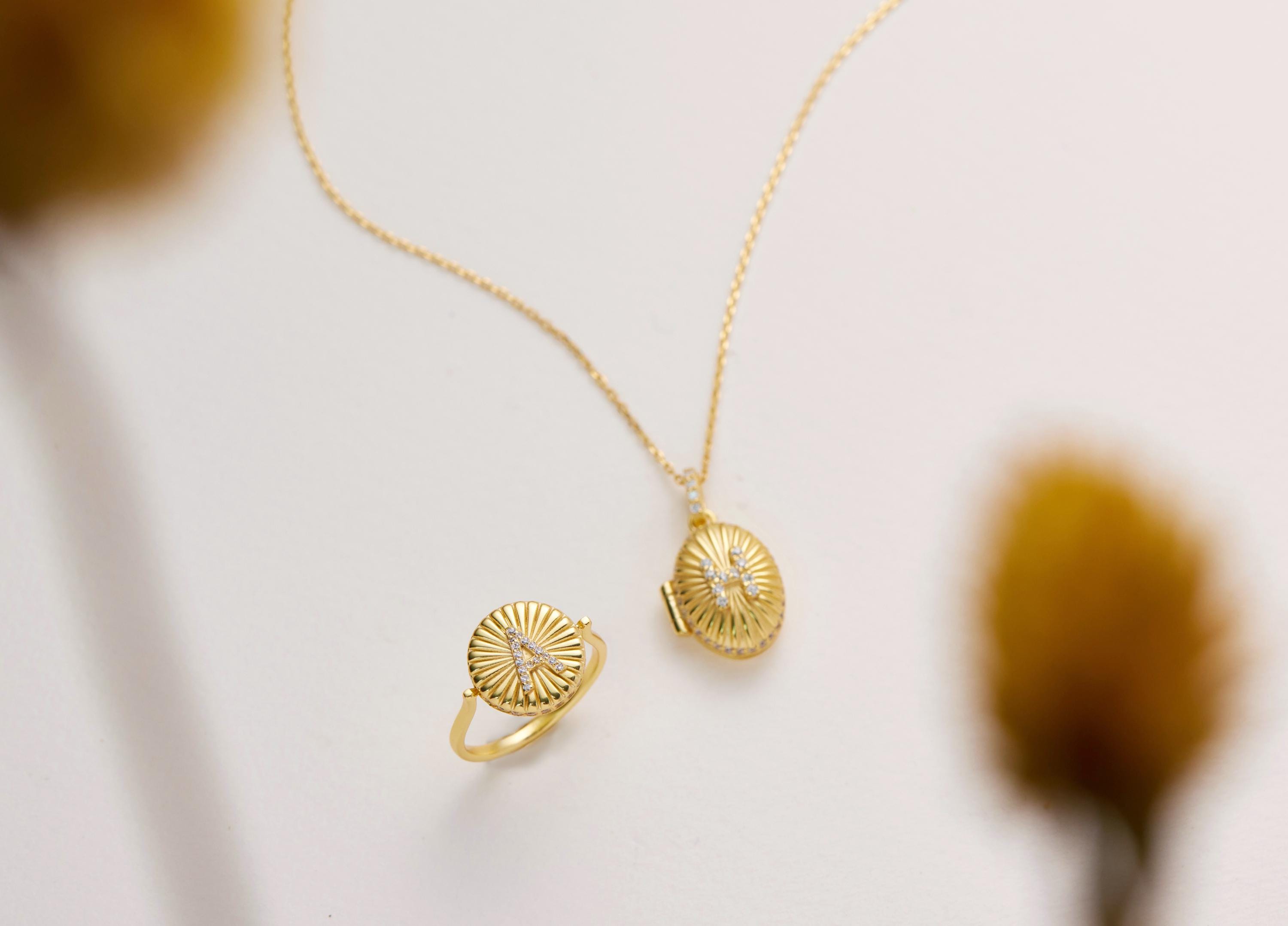 a gold necklace and a gold ring with a sunburst design, both placed on a white background.