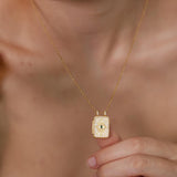 A close-up of a person&#39;s neck and chest wearing a gold necklace with a small square pendant.