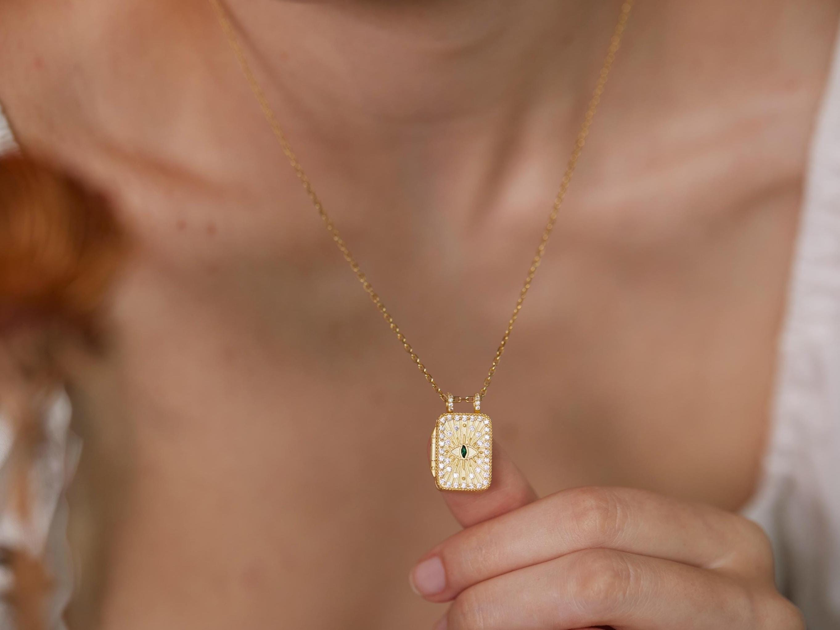 A close-up of a person&#39;s neck and chest wearing a gold necklace with a small square pendant.