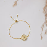 Gold bracelet with a sunflower charm on a light background