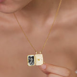 A person is holding a gold-colored locket pendant with a photo inside, which appears to be a small picture frame.