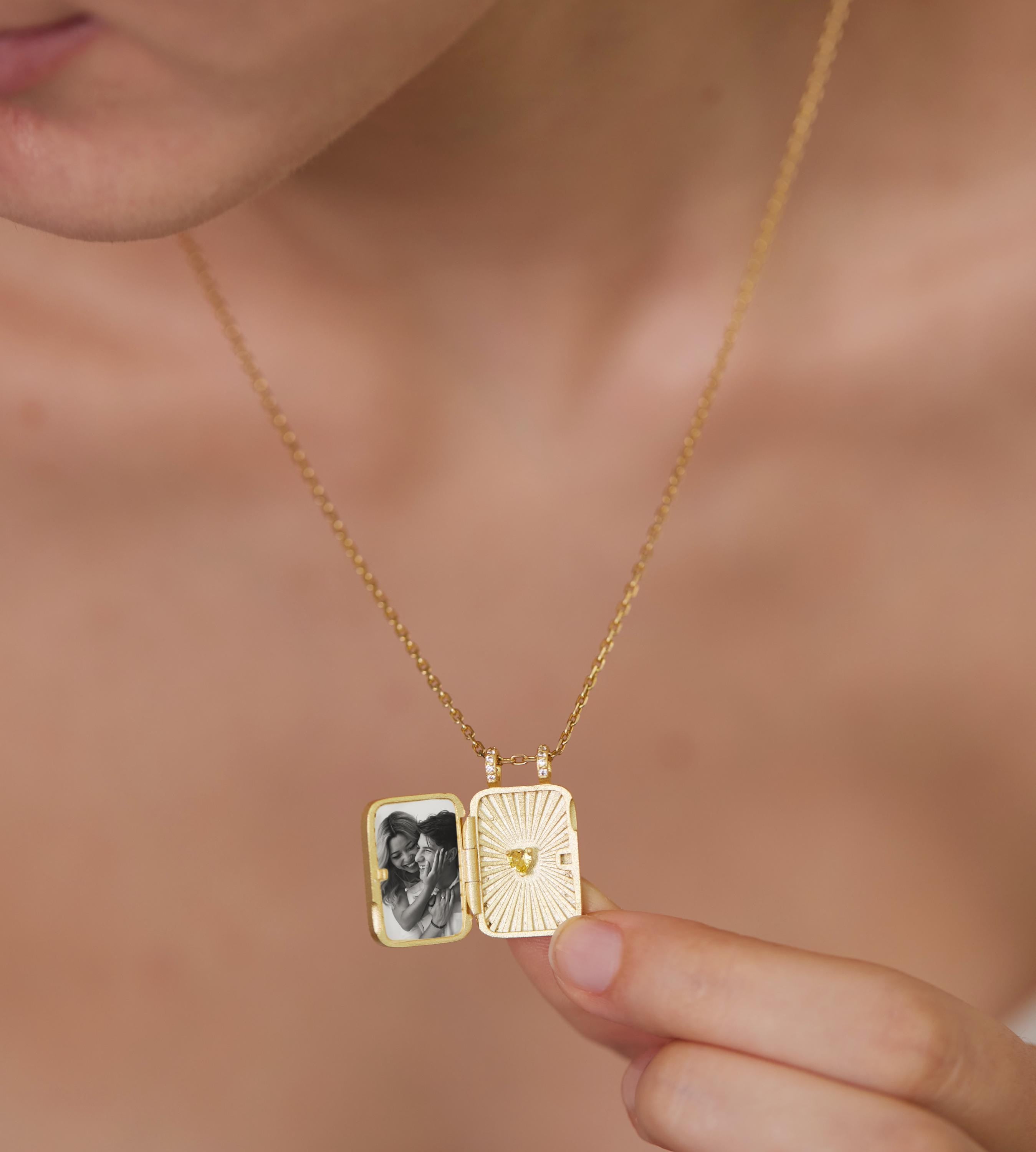 A person is holding a gold-colored locket pendant with a photo inside, which appears to be a small picture frame.