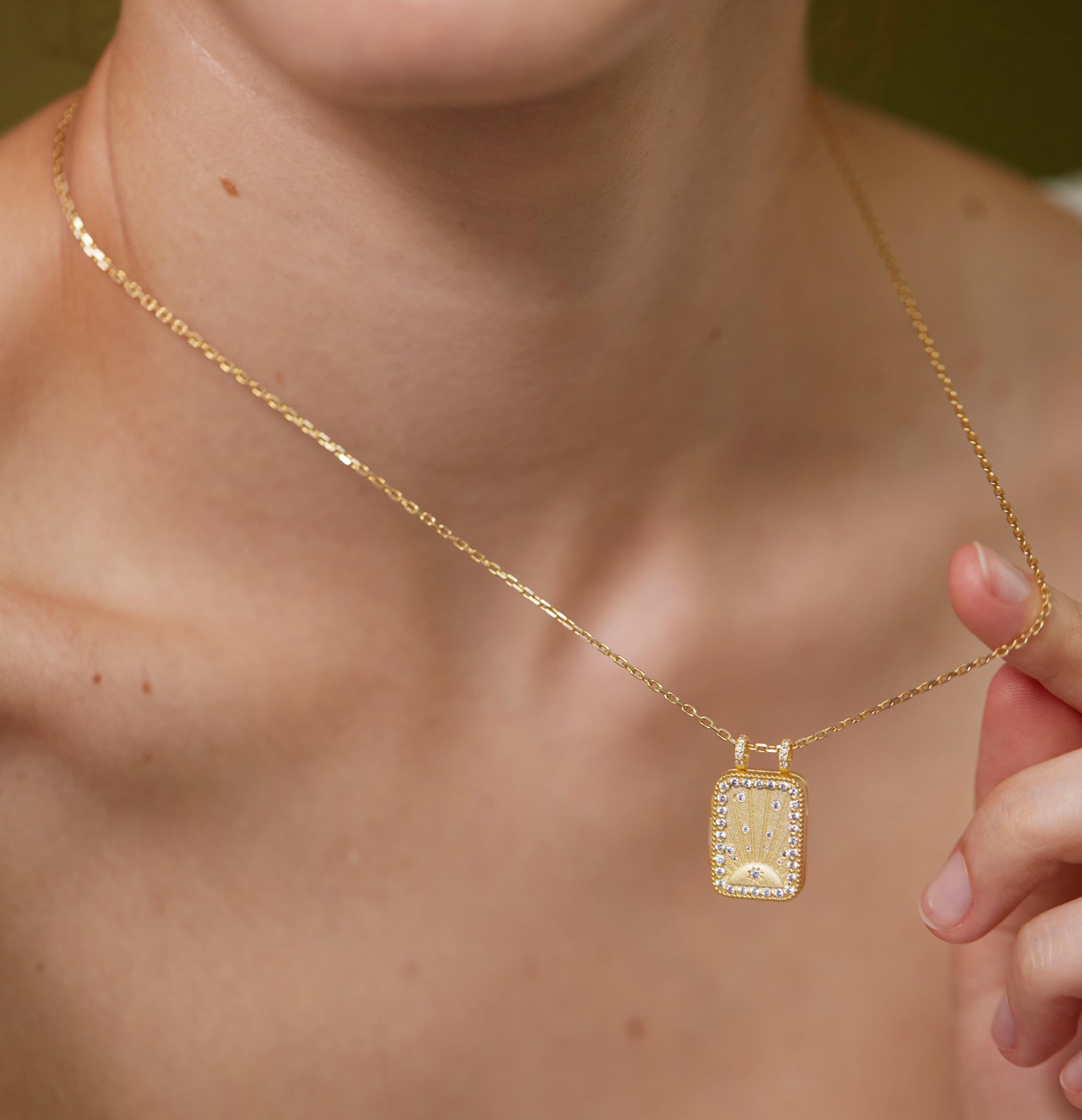 A close-up of a person's neck and chest wearing a gold necklace with a pendant.