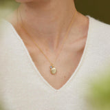 Gold necklace with a pendant worn by a person in a white sweater.