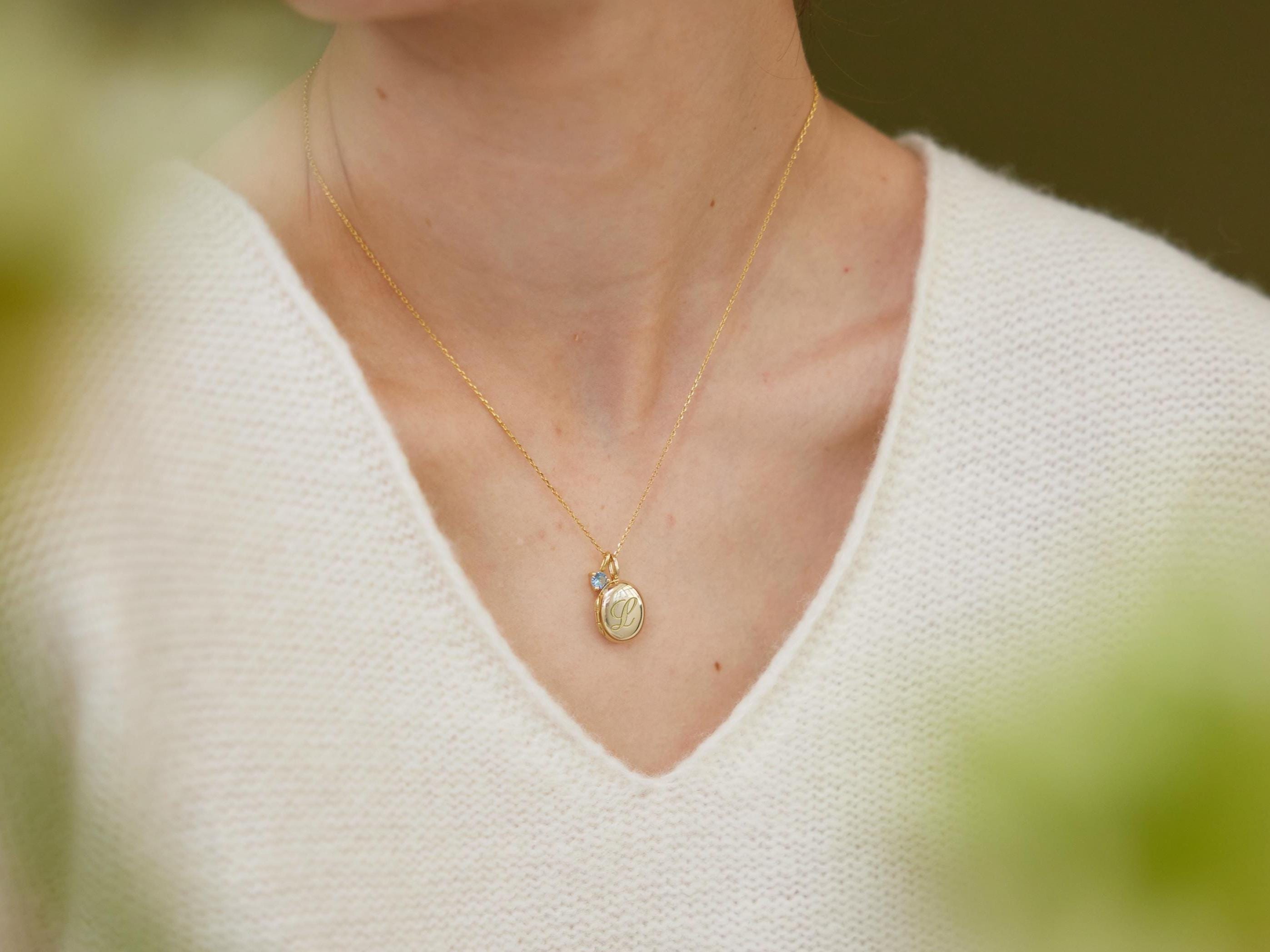 Gold necklace with a pendant worn by a person in a white sweater.