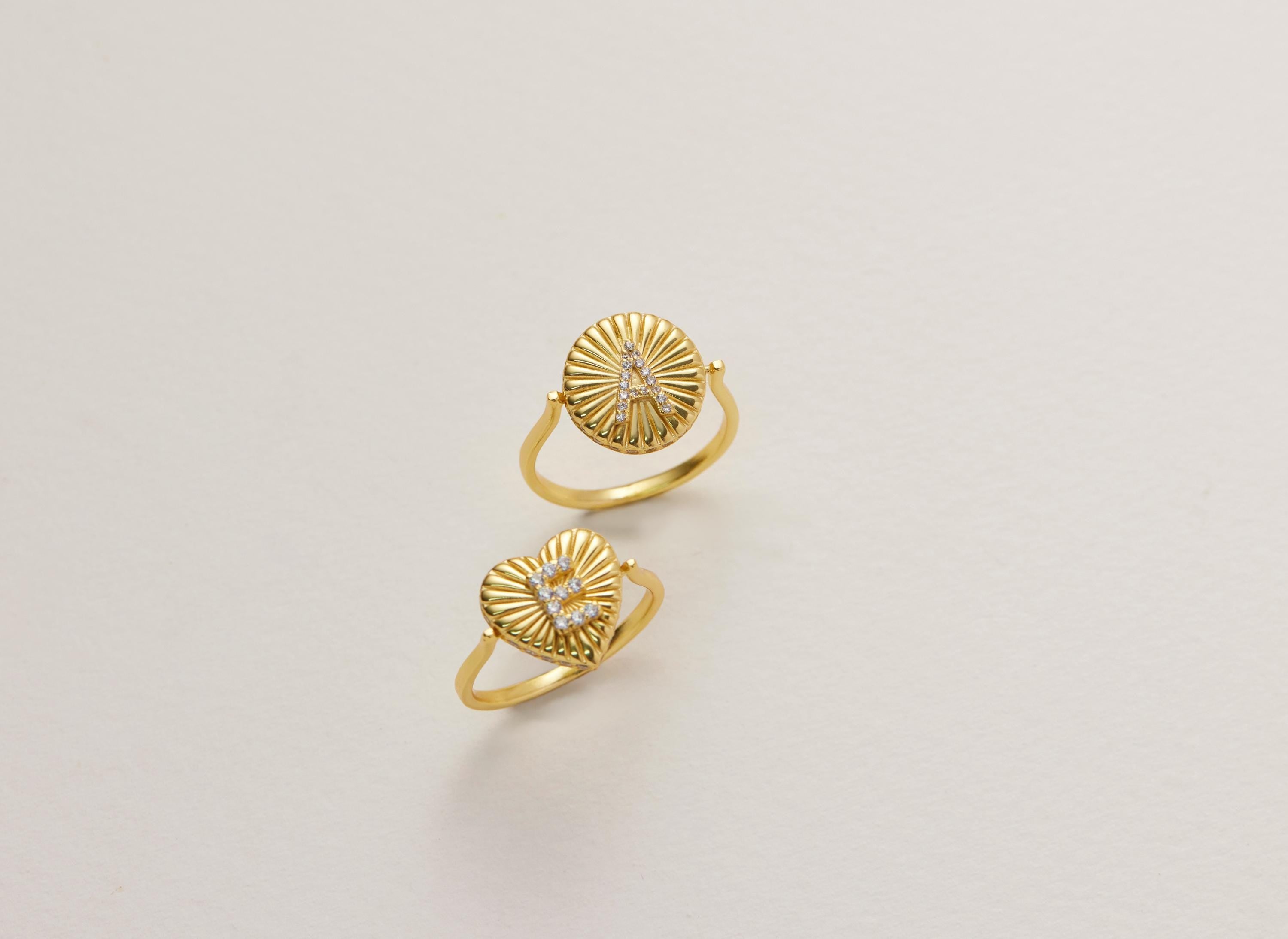 Two gold rings with a sunburst design and a heart-shaped gemstone are displayed against a white background.