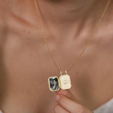A person is holding a gold-colored necklace with a small, rectangular pendant that contains a black and white photograph.