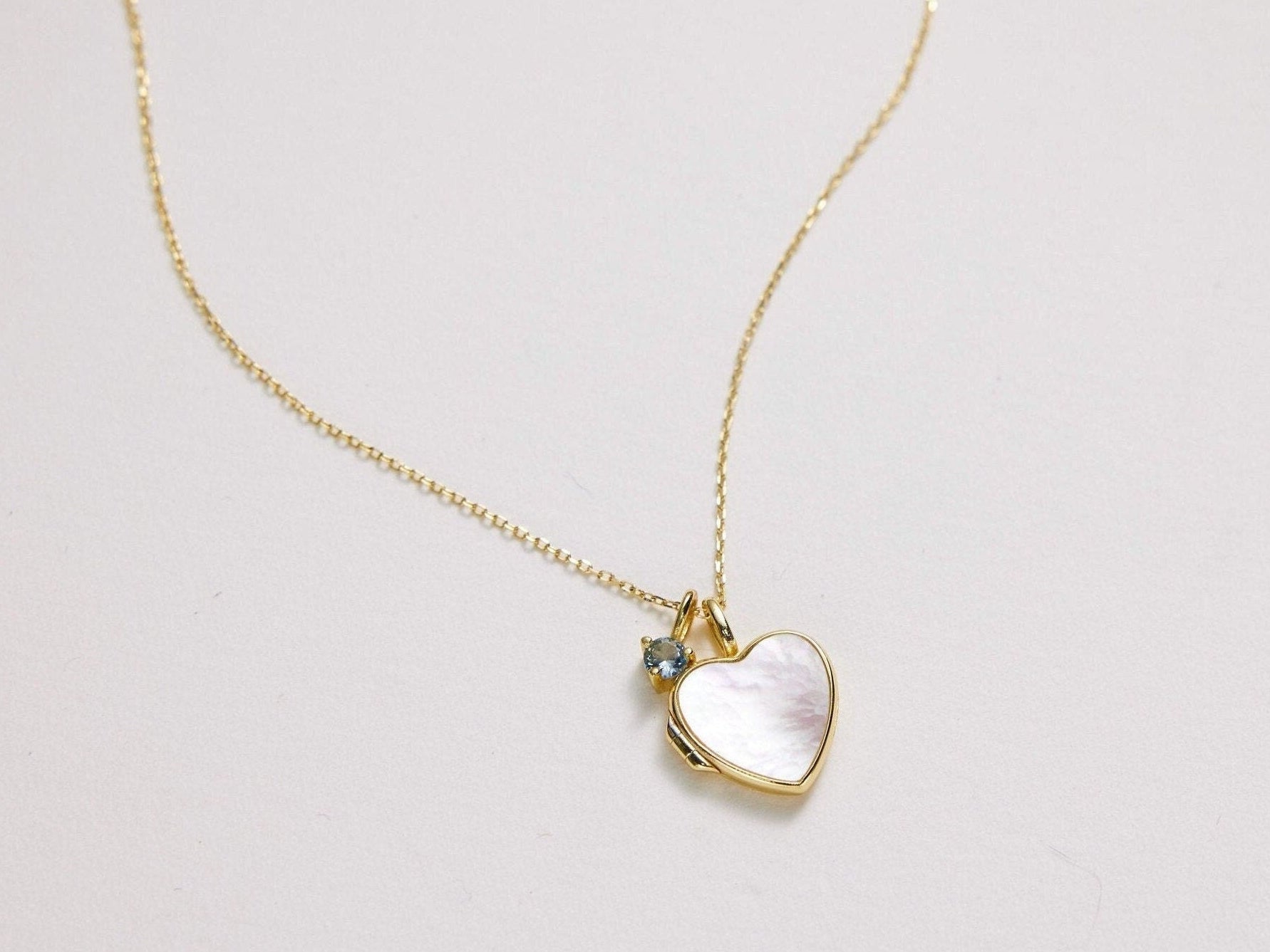 Gold necklace with a heart-shaped pendant on a light gray background