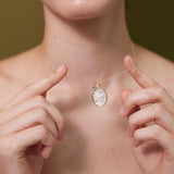 Person wearing a delicate necklace with a pendant, holding it with their hands.