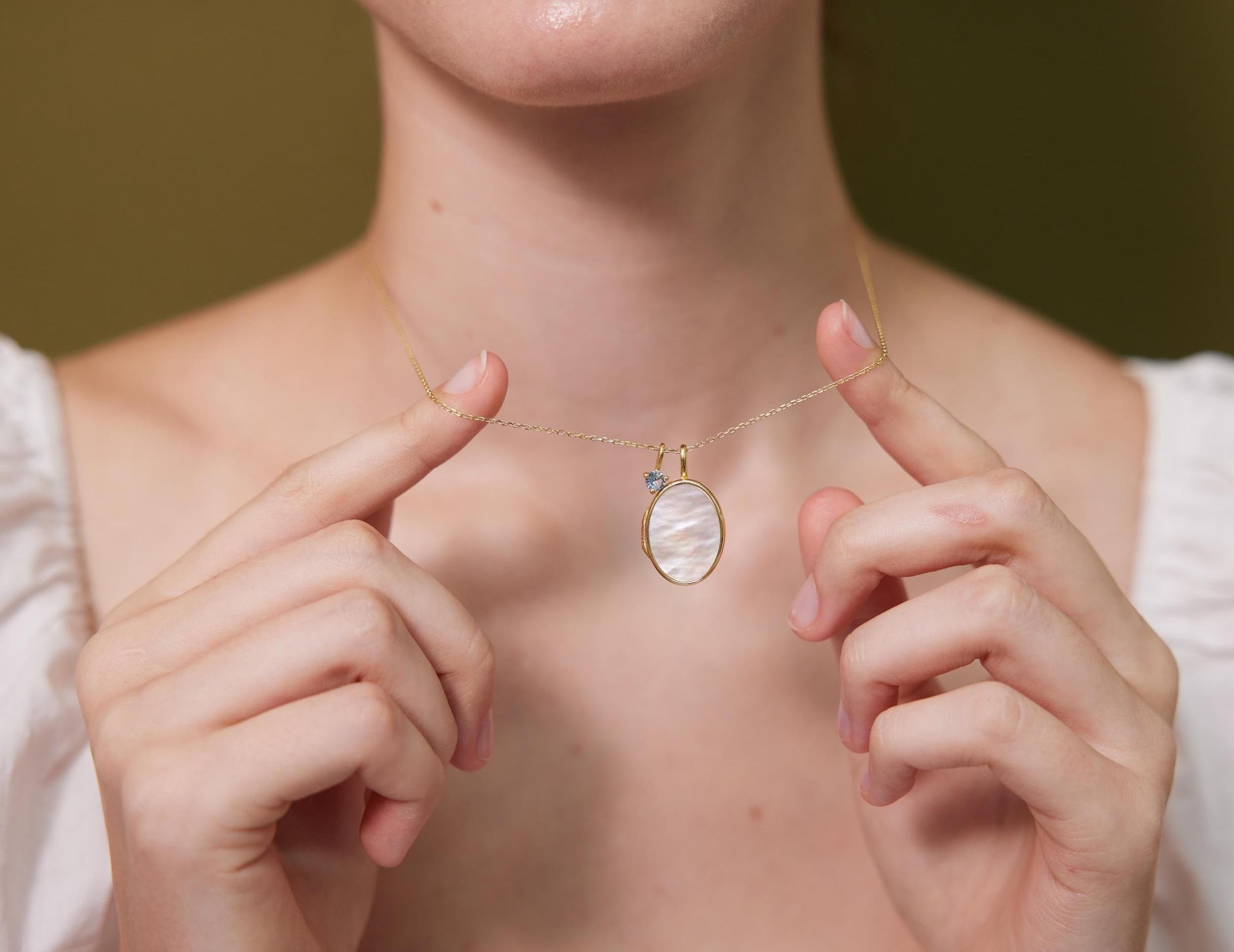 Person wearing a delicate necklace with a pendant, holding it with their hands.
