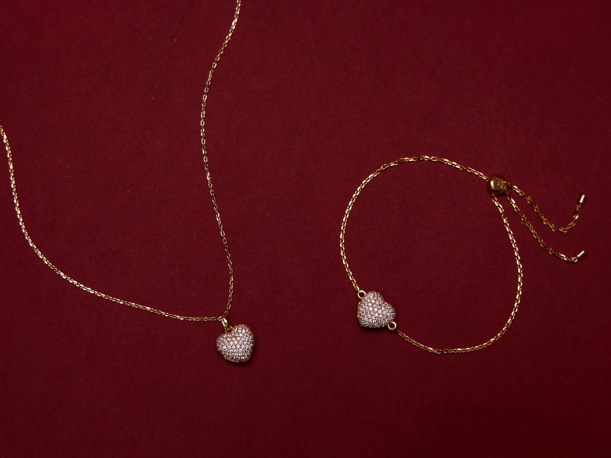 Gold necklace and bracelet with heart-shaped pendants on a red background