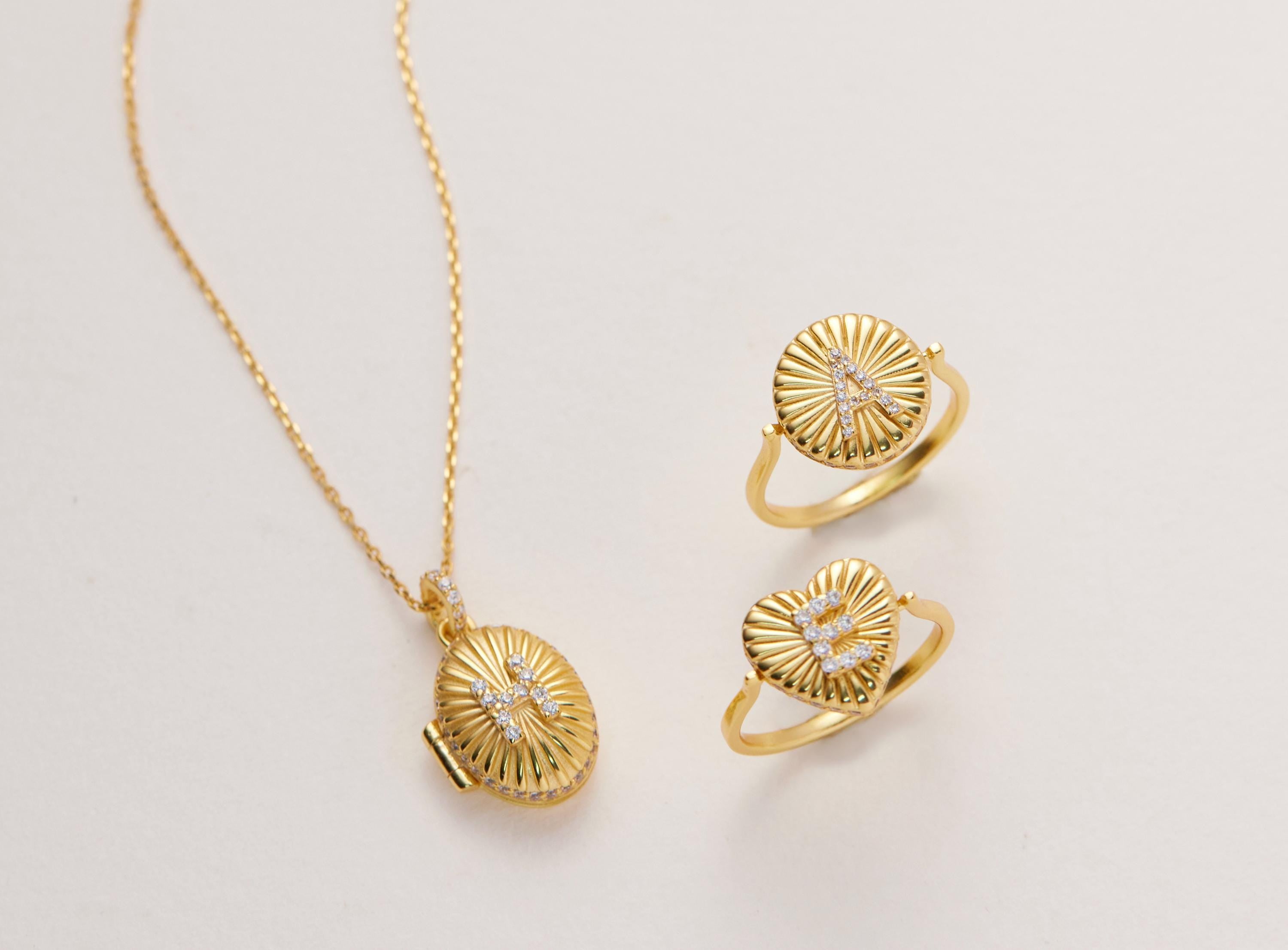 A gold necklace with a pendant and two gold rings with heart-shaped designs are displayed on a white background.