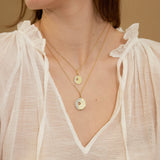 Close-up of a person wearing two gold necklaces with pendants against a neutral background
