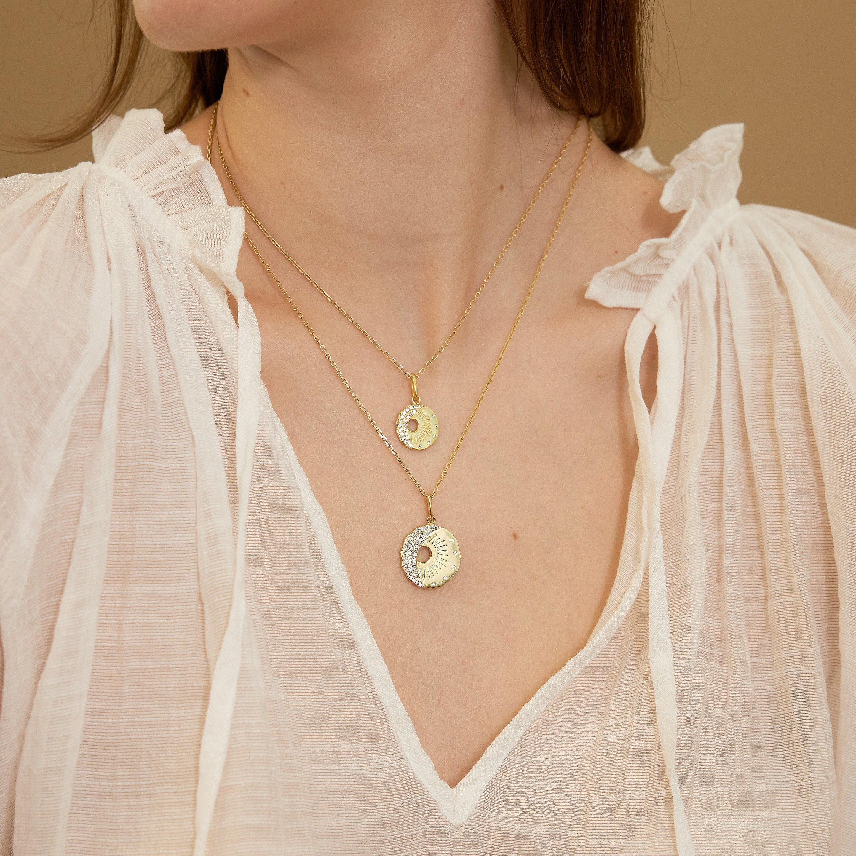 Close-up of a person wearing two gold necklaces with pendants against a neutral background